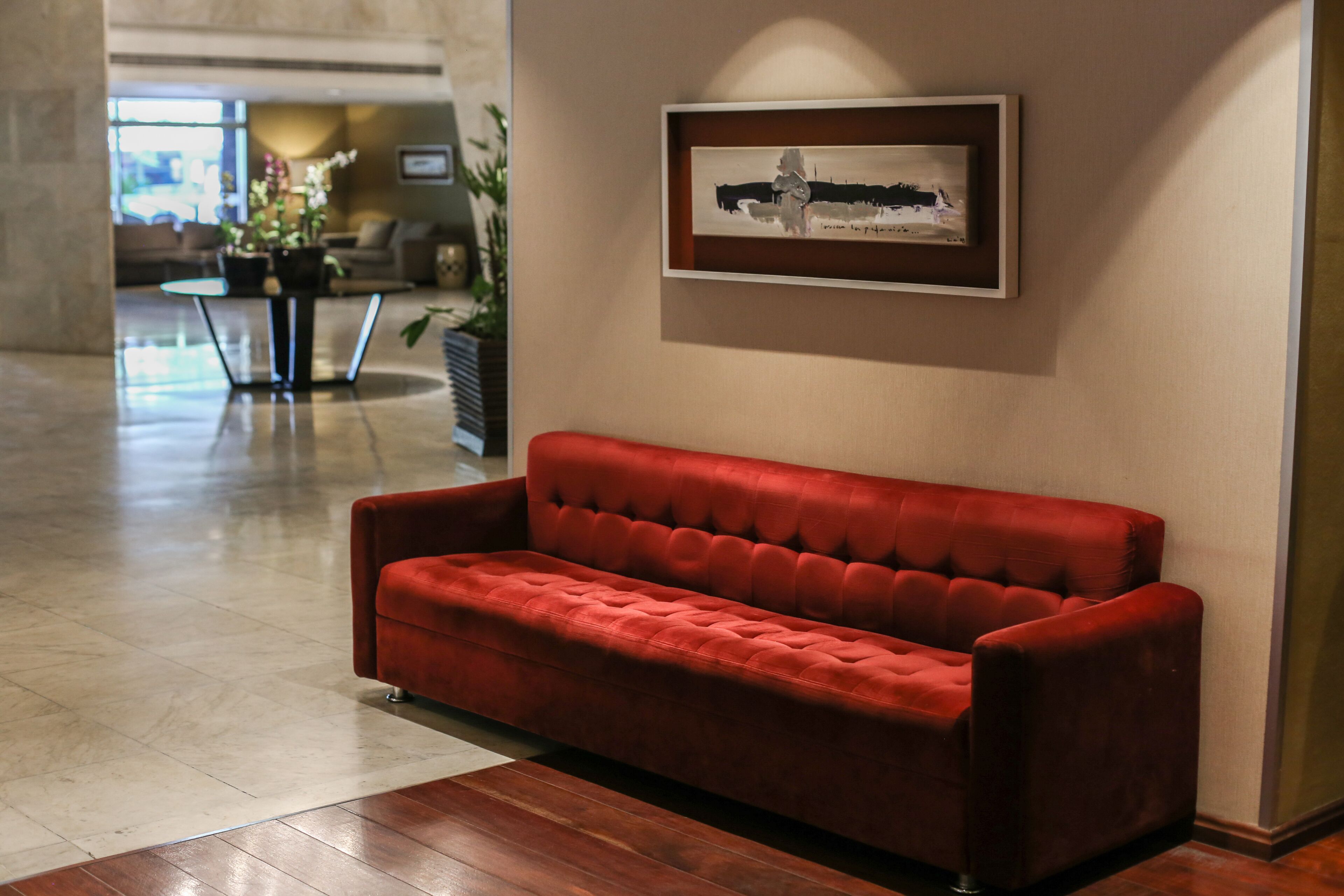 A red velvet sofa in a lobby with a framed artwork on the wall and a potted plant in the background.