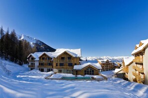A snow-covered resort with wooden buildings, a pool, and mountains in the background. - La Combe d'Or (Les Orres)