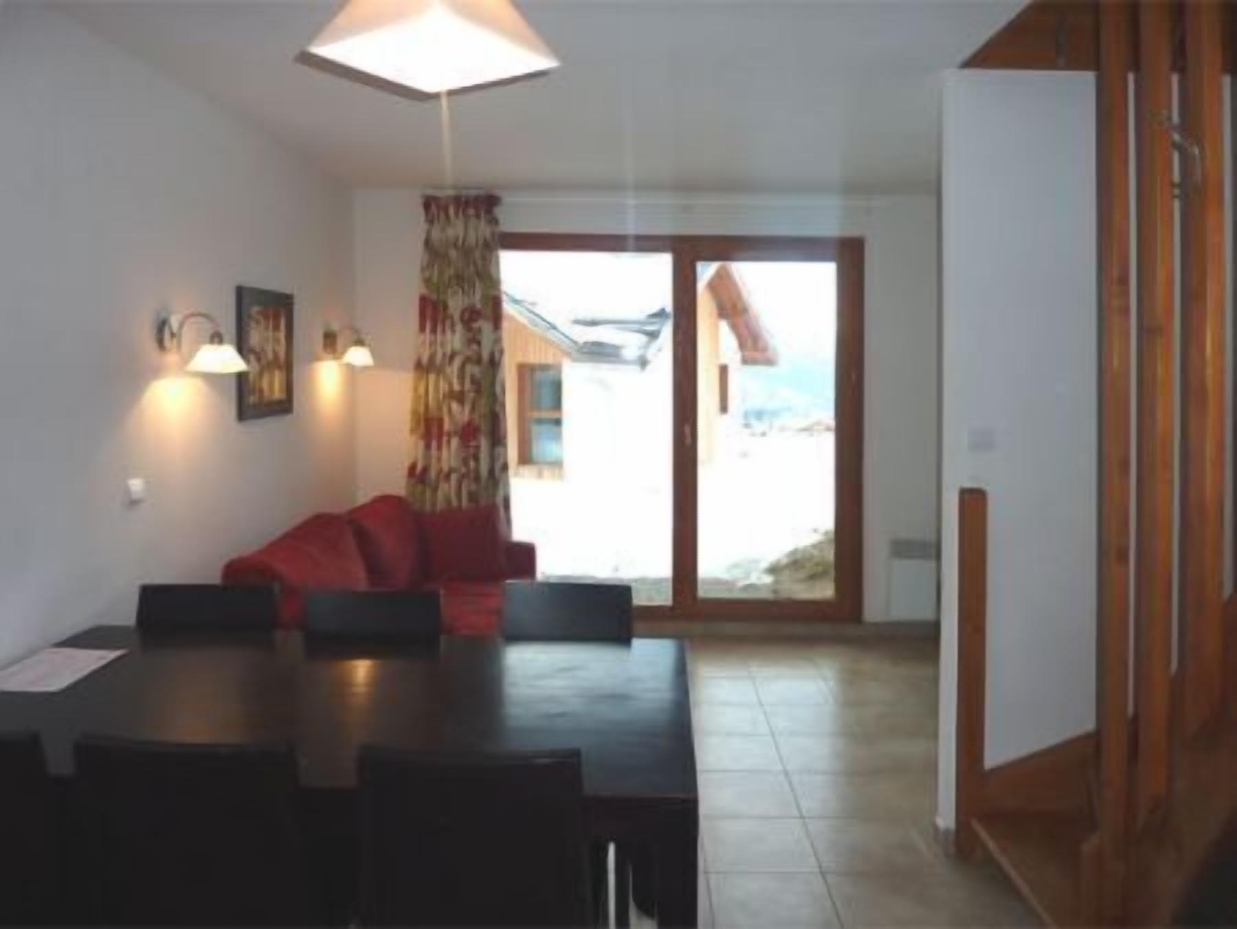 A dining area with a table and chairs, a red sofa, and a window with a view of a building.