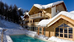 Eine Holzhütte mit Pool, umgeben von Schnee, vor blauem Himmel.