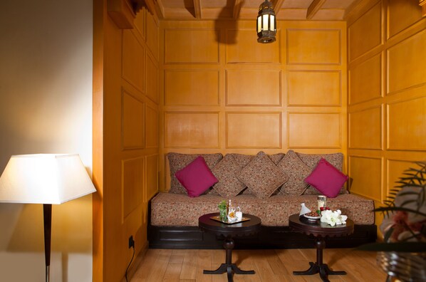 Una habitación con un revestimiento de madera, un sofá con cojines estampados, una lámpara y dos mesitas con adornos.