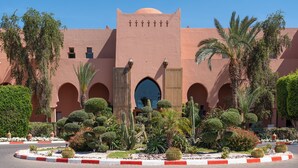 Un edificio con un arco central, rodeado por un jardín ajardinado con diversas plantas y cactus.