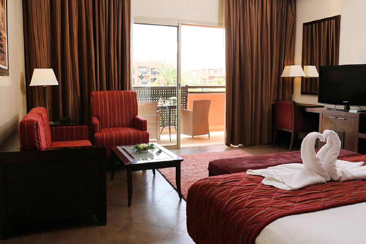 Habitación de hotel con cama, escritorio, silla, sofá, balcón y vistas, además de televisor.