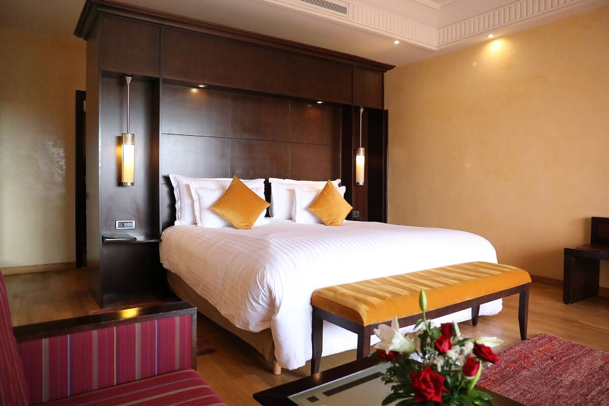 Habitación de hotel con una cama grande, lámparas de noche, un banco y un arreglo floral.