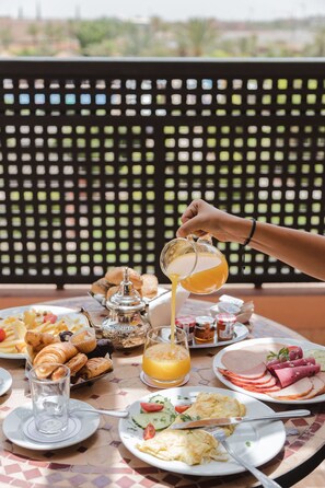 Une table de petit-déjeuner avec des croissants, du jambon, des œufs et du jus d’orange.