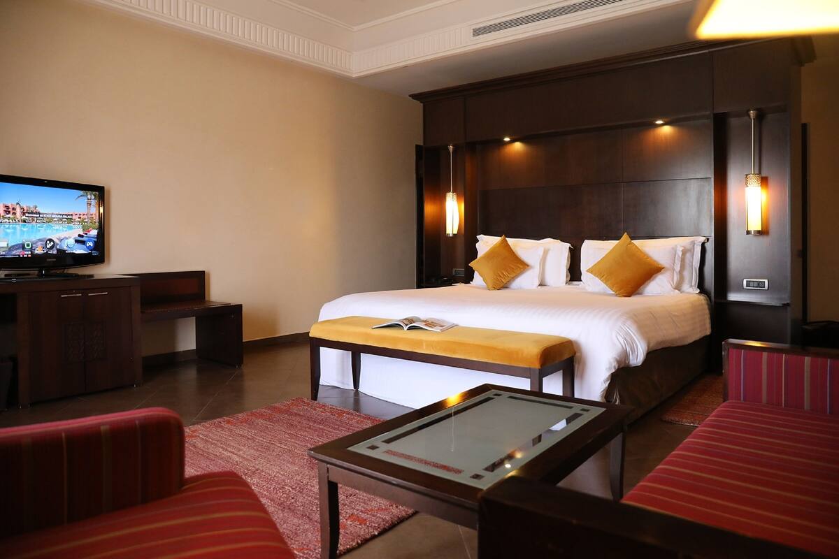Una habitación de hotel con una cama grande, lámparas de noche, un televisor, un escritorio pequeño y un sofá a rayas rojas.