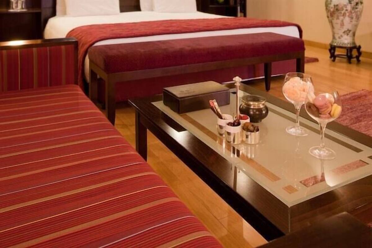 Una habitación de hotel con una cama grande, un sofá, una mesita con aperitivos y un jarrón decorativo.