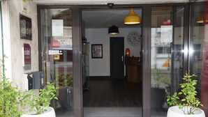 A hotel entrance with a modern design, including a glass door, a clock, and a visible interior with a wooden floor and a hanging light fixture.