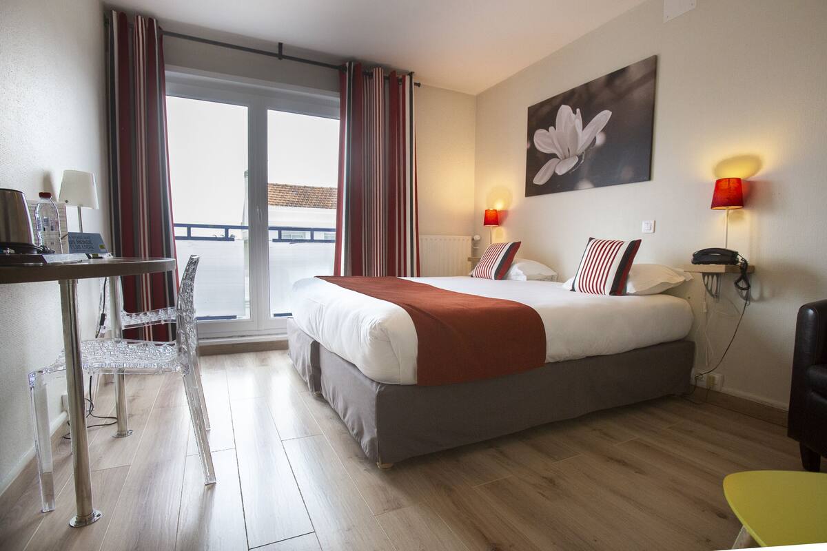 Una habitación de hotel con cama, escritorio, silla, lámpara y vistas al exterior.
