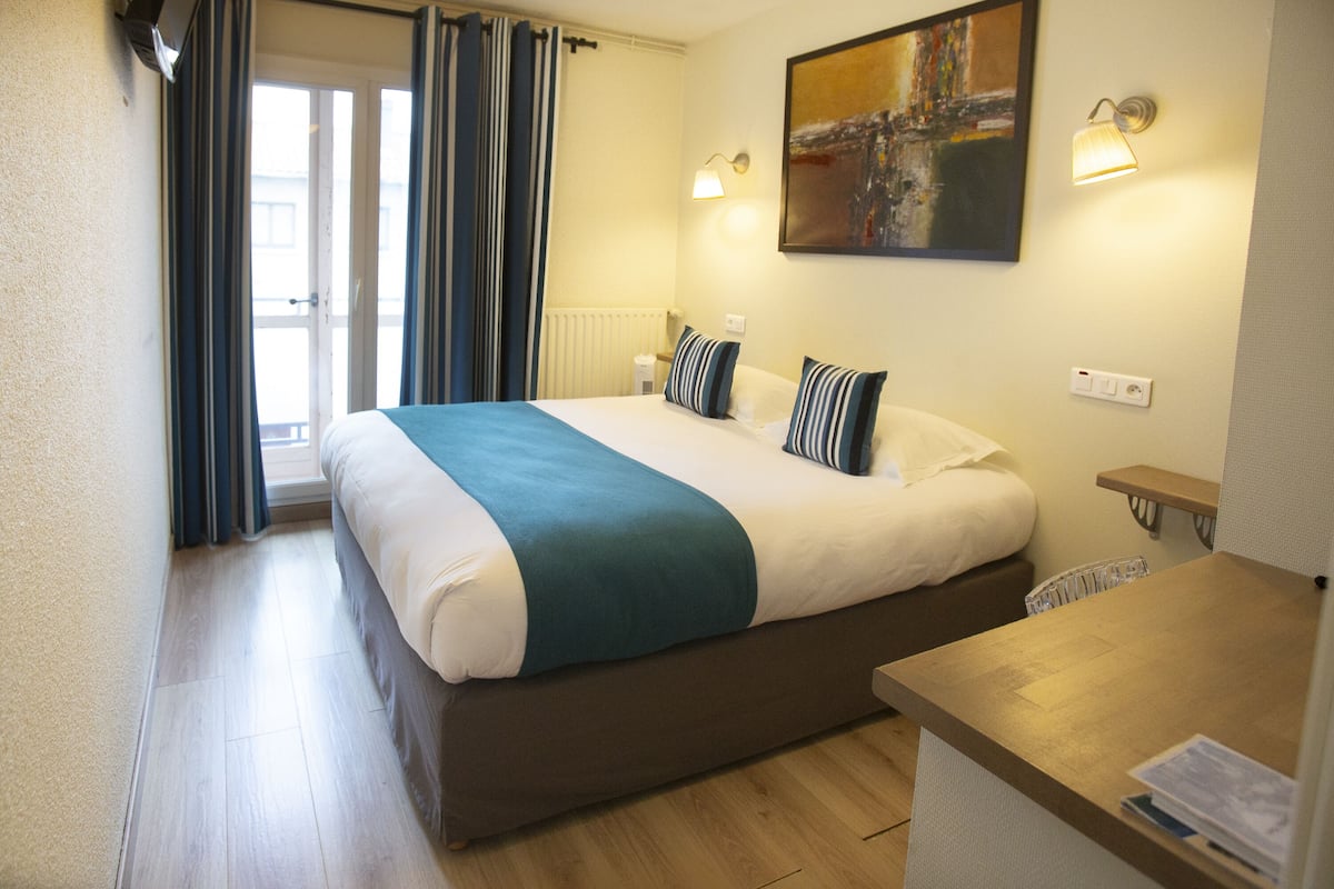 Habitación de hotel con una cama grande, una mesita de noche, un escritorio y una ventana con cortinas.