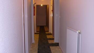 A hallway with a carpeted floor, white walls, and a white radiator on the right.