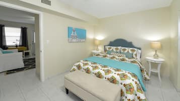 A bedroom with a bed, two bedside tables with lamps, a bench, a painting of the Eiffel Tower, and a dining area with a table and chairs.