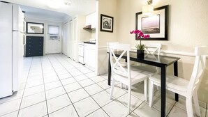 Una cocina moderna con armarios blancos, encimera negra y comedor con mesa de vidrio y sillas blancas.