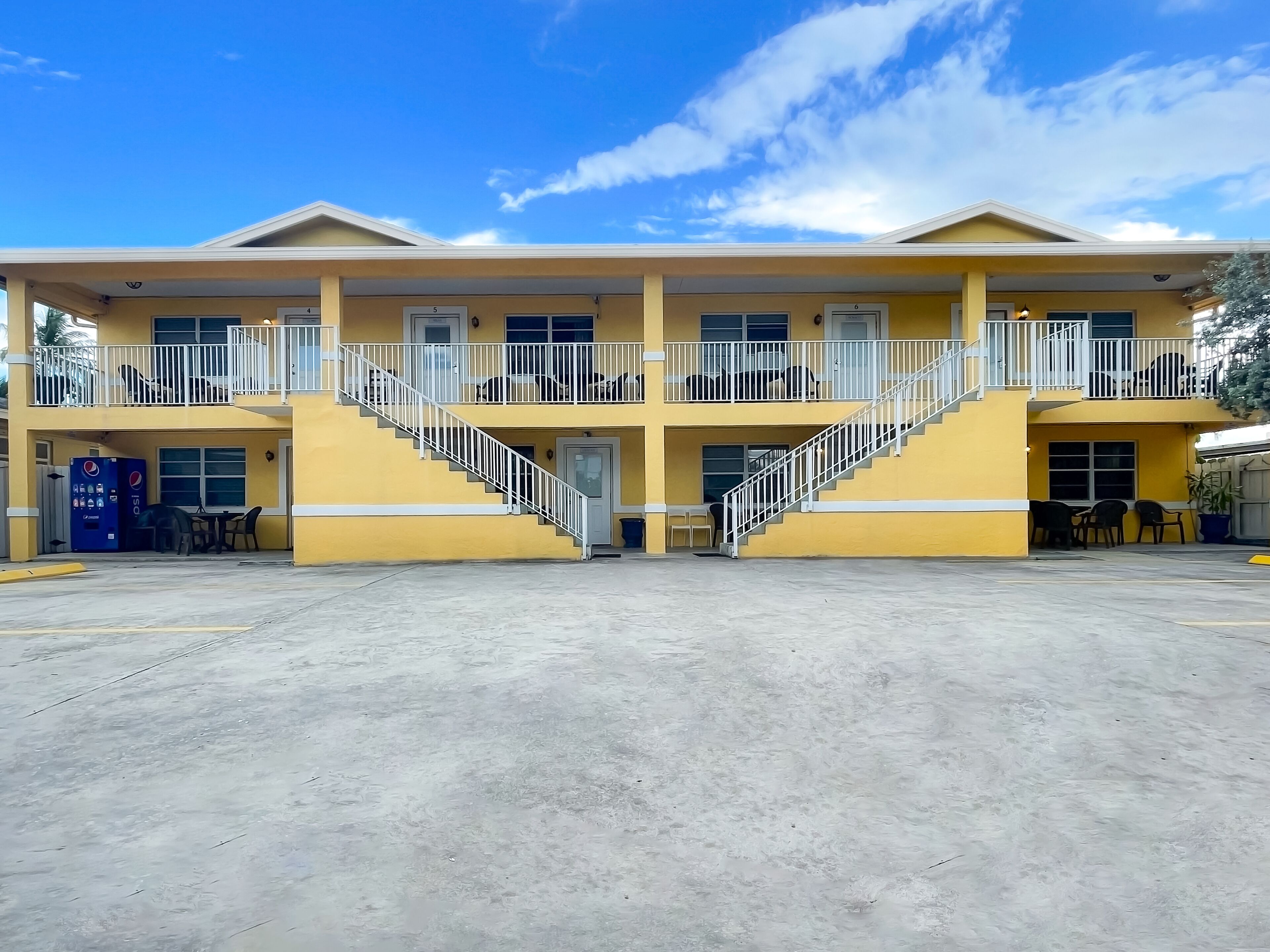 A two-story motel with a central staircase, outdoor seating, and a vending machine.