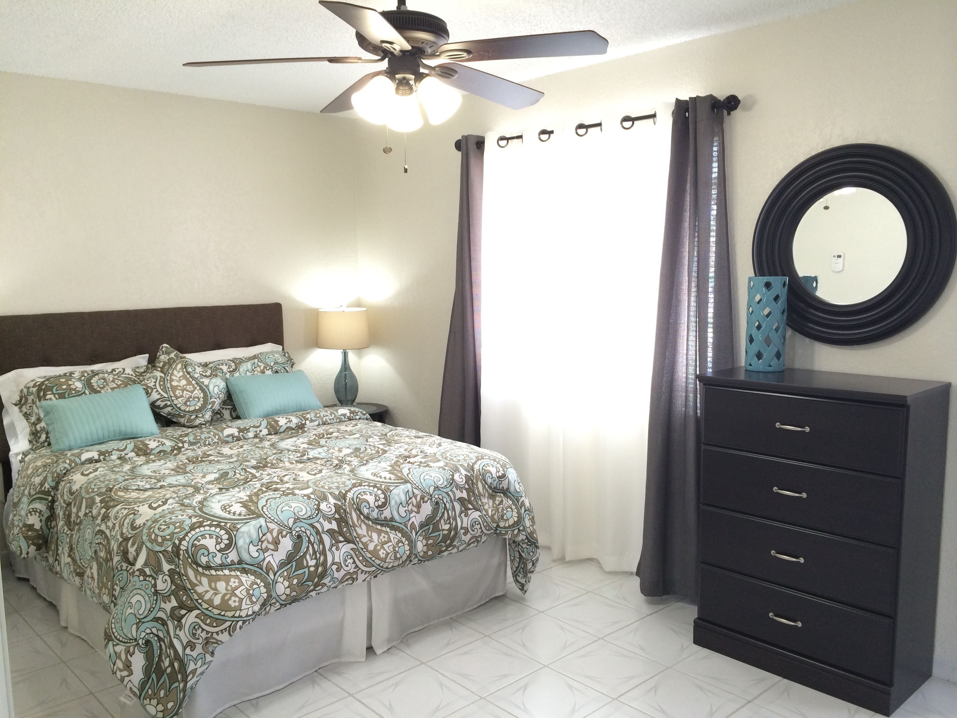 A bedroom with a bed, a nightstand, a dresser, a ceiling fan, and a mirror.
