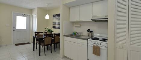 Una cocina con armarios blancos, una estufa y una zona de comedor con mesa y sillas.
