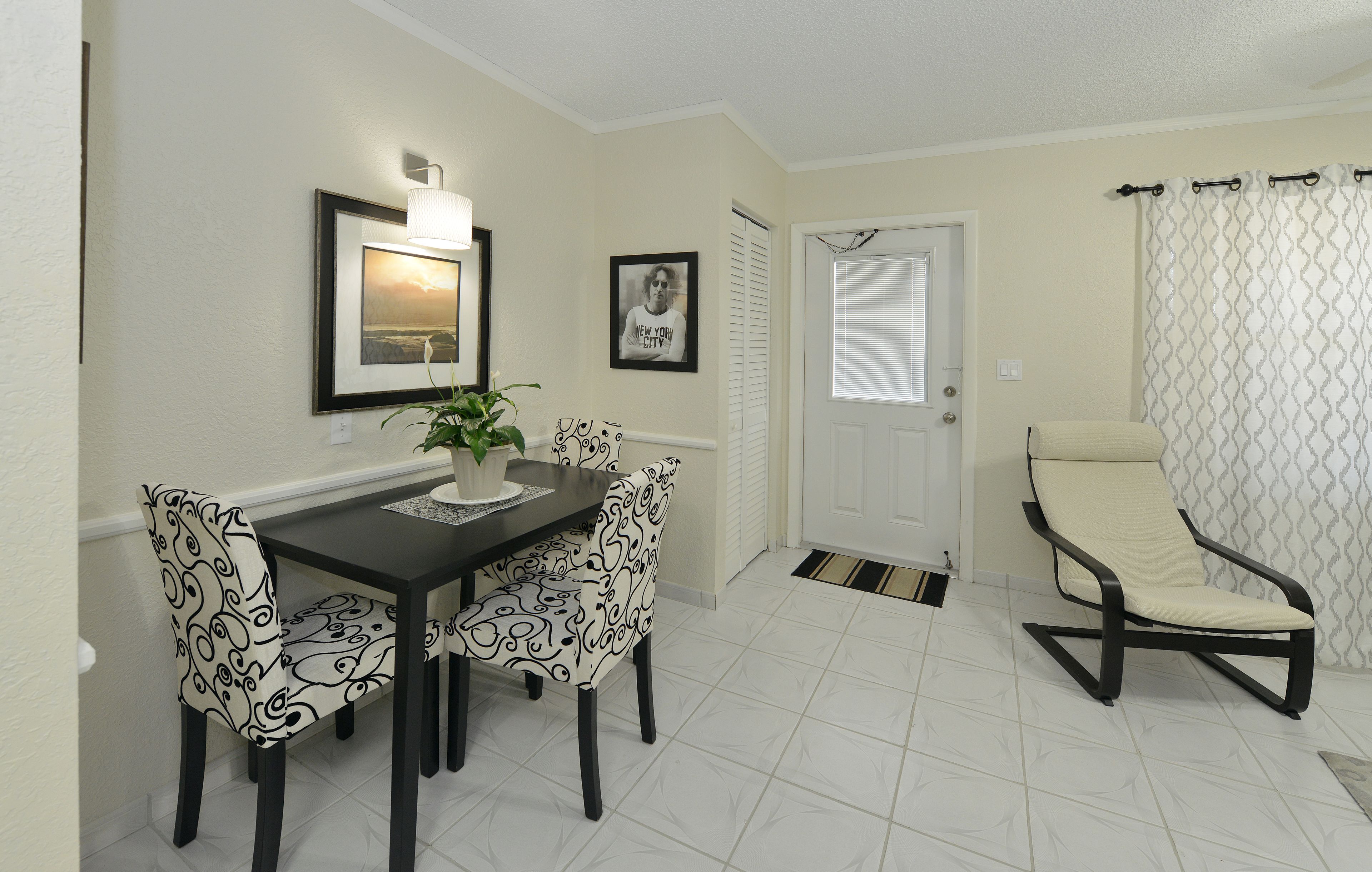 A dining area with a table and chairs, a potted plant, framed pictures on the wall, and a door with a curtain.