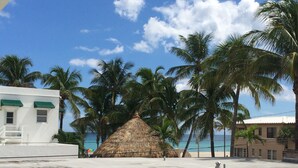 Un edificio frente a la playa con una estructura de techo de paja, palmeras y vista al océano.