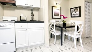 Una cocina compacta con armarios blancos, una estufa y una zona de comedor con una mesa negra y sillas blancas.