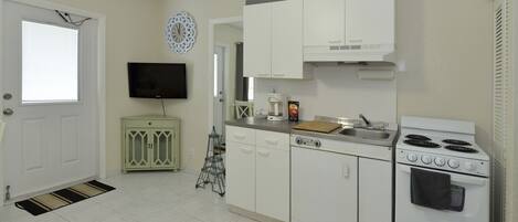 A kitchen with white cabinets, a stove, a sink, and a television on the wall.