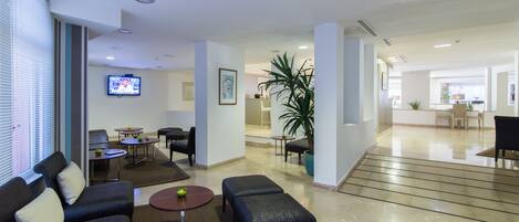 A spacious lobby with a sofa, chairs, a small table, and a potted plant.