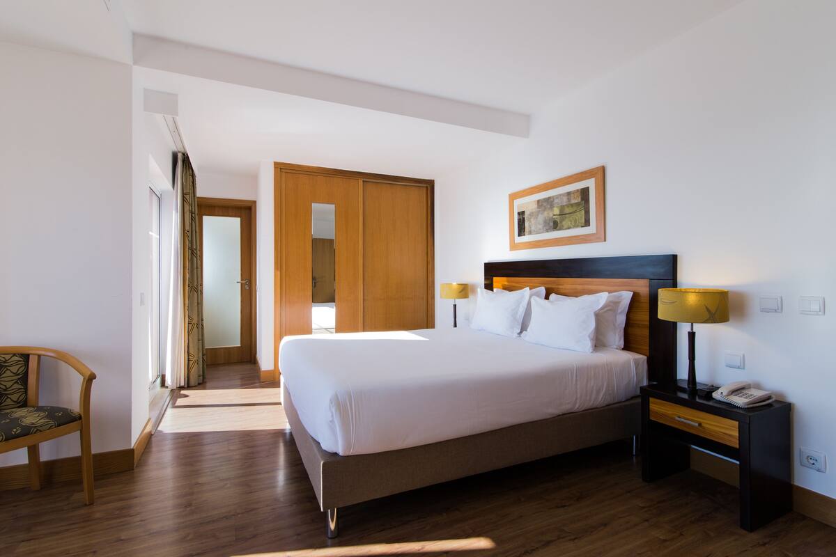 Une chambre d’hôtel avec un grand lit, une armoire en bois, une table de chevet avec une lampe et une chaise.