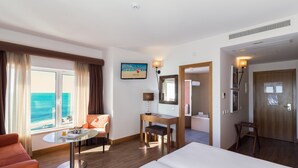 Une chambre d’hôtel avec un grand lit, un bureau avec une chaise, une petite table avec une chaise, une télévision et une vue sur l’océan.