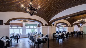 Une salle à manger spacieuse, dotée de hauts plafonds en arc de cercle et de grandes fenêtres. Les tables sont disposées avec des chaises, et la pièce présente un design moderne, tout en conservant un certain cachet rustique.