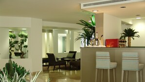 Un hall d’hôtel moderne avec un bar, des espaces pour s’asseoir et des plantes décoratives.