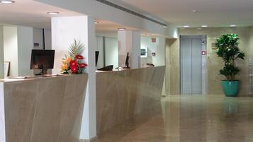 A modern reception area with a marble reception desk, a computer monitor, and a potted plant.
