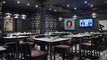 A restaurant with tables and chairs, a television screen, and bookshelves.