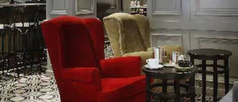 A bar area with a patterned floor, a red armchair, a beige armchair, and a small round table with a drink.