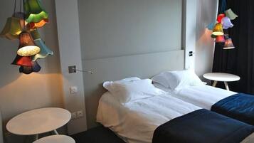 A hotel room with a bed, two white round tables, and colorful hanging lamps.