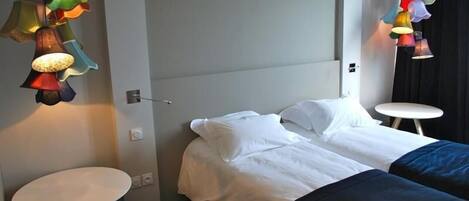 A hotel room with a bed, two white round tables, and colorful hanging lamps.