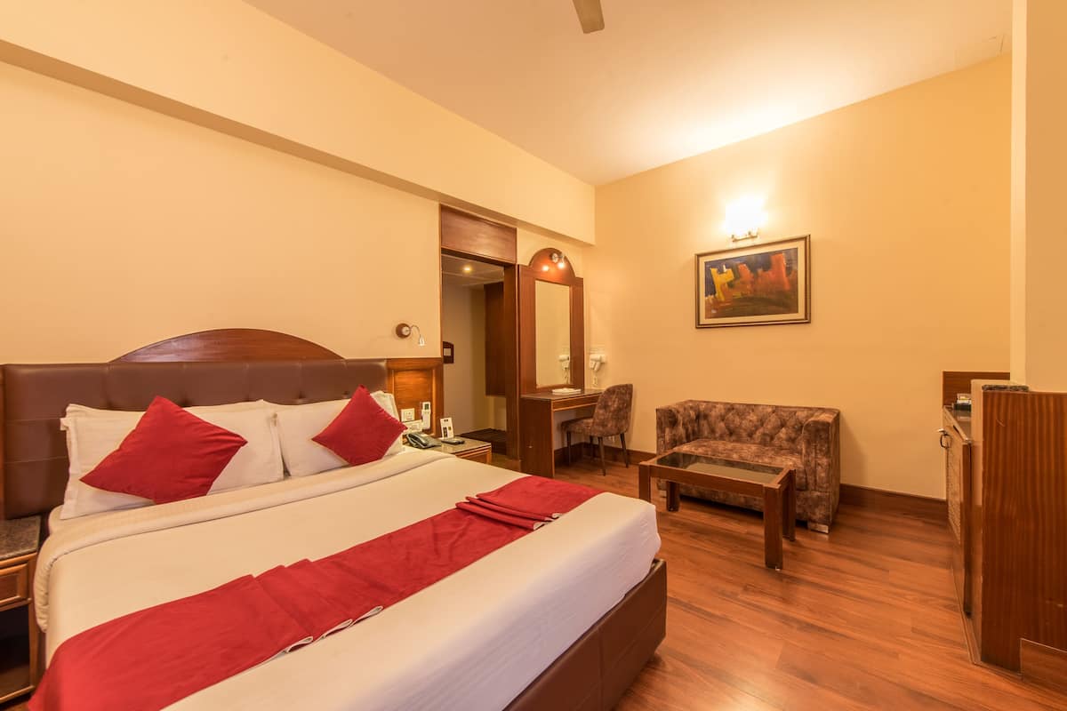 A hotel room with a large bed, a desk, a chair, and a painting on the wall.