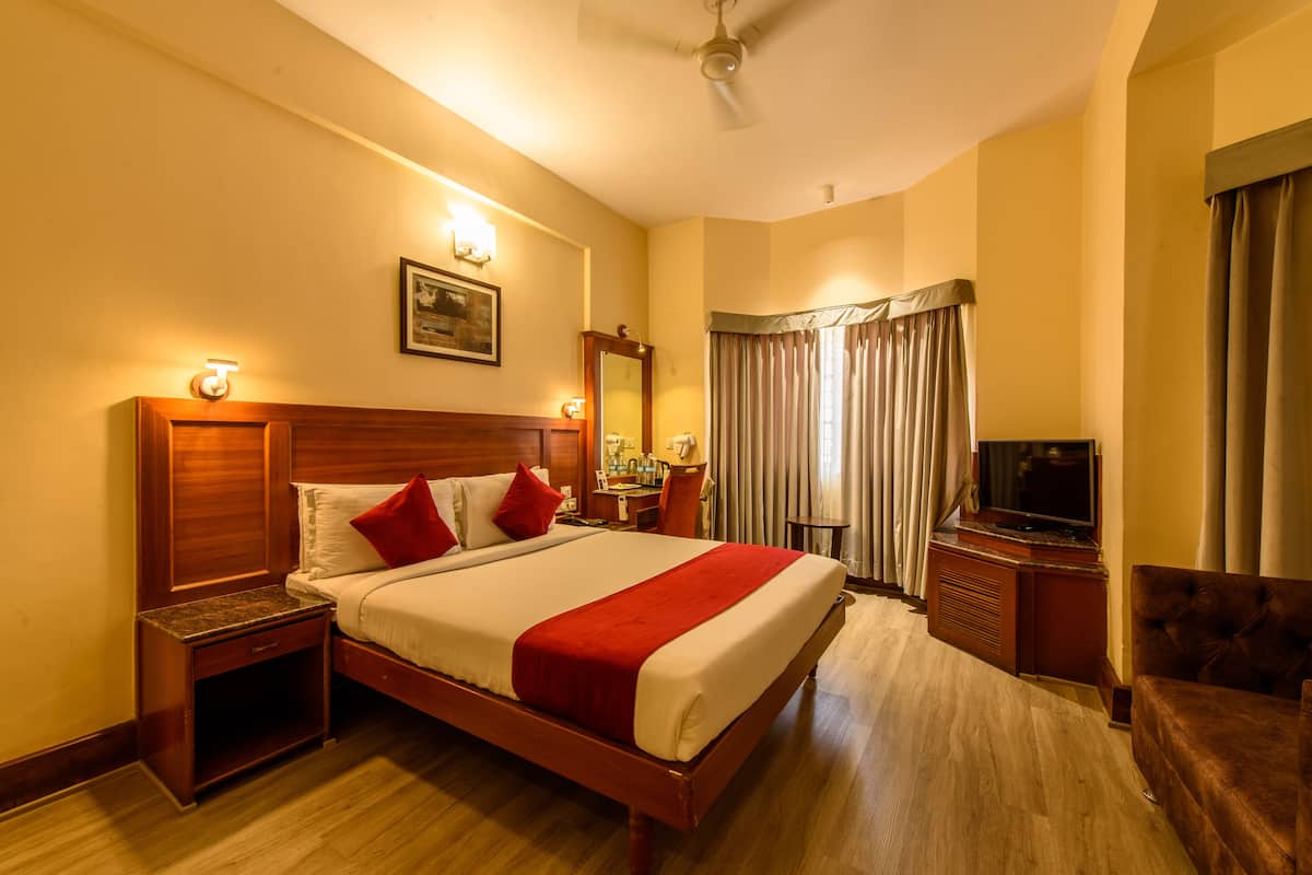 A hotel room with a large bed, wooden headboard, bedside tables, a TV, and a desk with a chair.