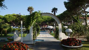 A pathway leading through a garden with a decorative archway, surrounded by lush greenery and red flowers. - Park Hotel Maracaibo (Jesolo)