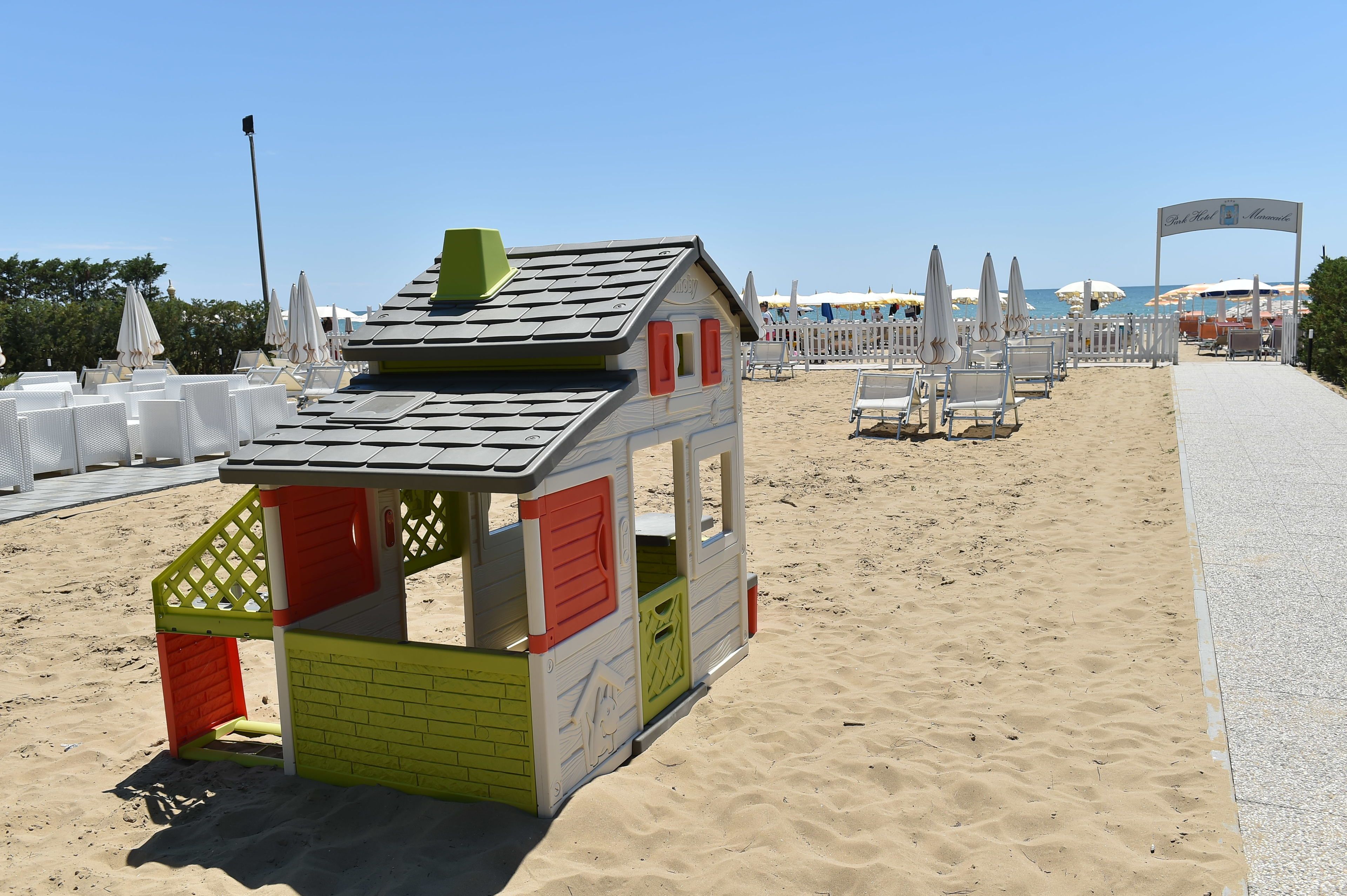 Una casetta sulla spiaggia con decorazioni rosse e verdi, circondata da sedie e ombrelloni.