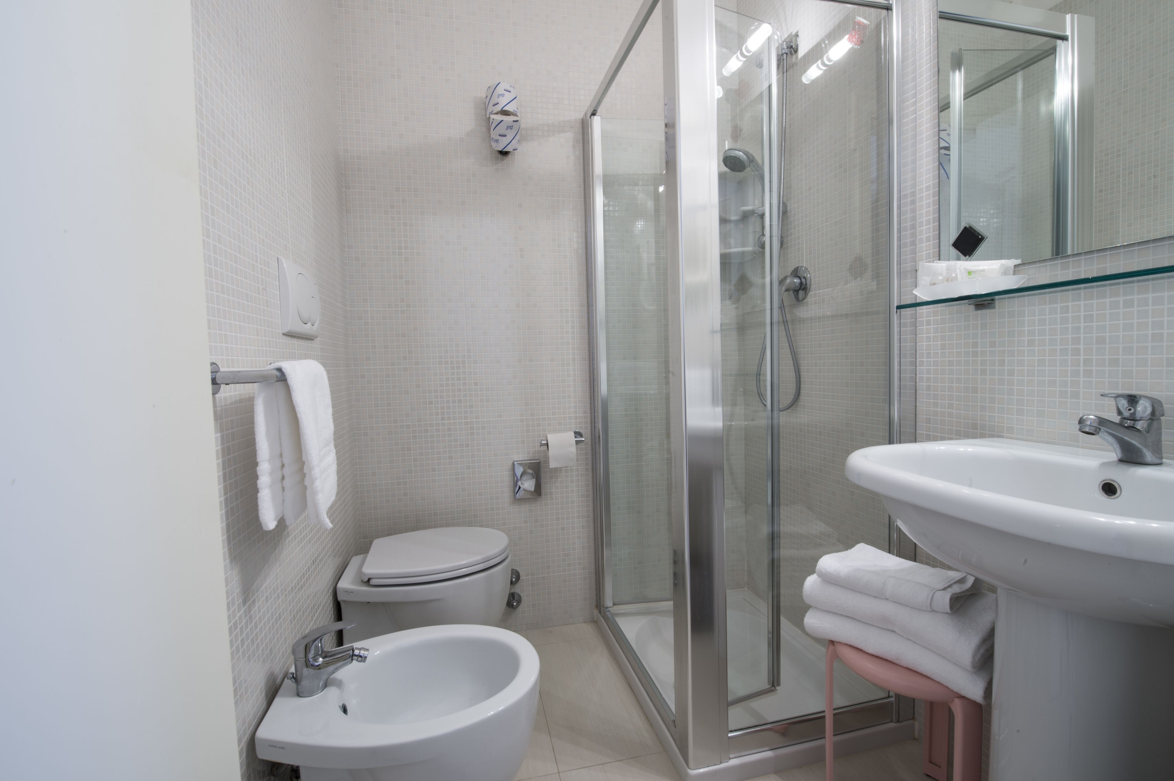 A modern bathroom with a toilet, bidet, sink, and glass shower enclosure.