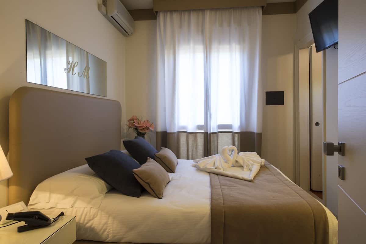Une chambre d’hôtel avec un grand lit, un téléviseur à écran plat, une table de chevet avec une lampe et une fenêtre avec des rideaux.