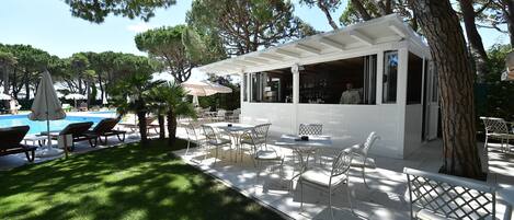 Uma área de pátio com mobiliário para áreas externas, piscina e um bar coberto.