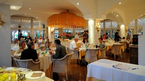 A spacious restaurant with high ceilings, arched windows, and a central orange chandelier. - Park Hotel Maracaibo (Jesolo)