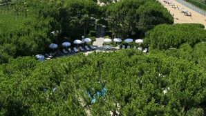 A resort with a pool area surrounded by lush greenery, a beach in the background, and a clear view of the sea. - Park Hotel Maracaibo (Jesolo)