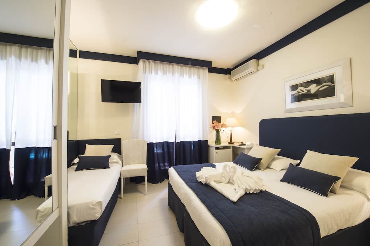 Une chambre d’hôtel avec deux lits, une télévision, un bureau avec une lampe et un tableau encadré au mur.