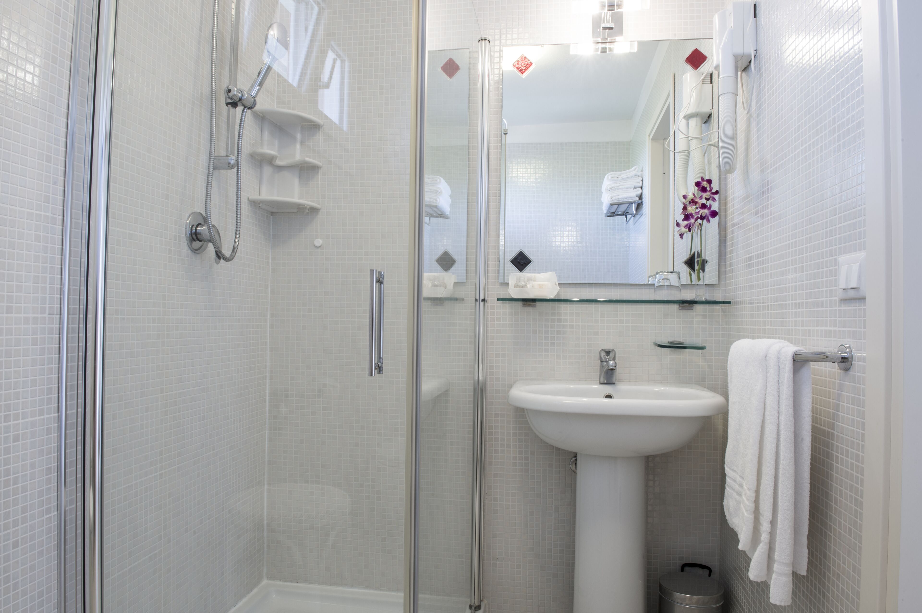 A modern bathroom with a glass shower enclosure, a white sink, and a mirror with a decorative tile backsplash.