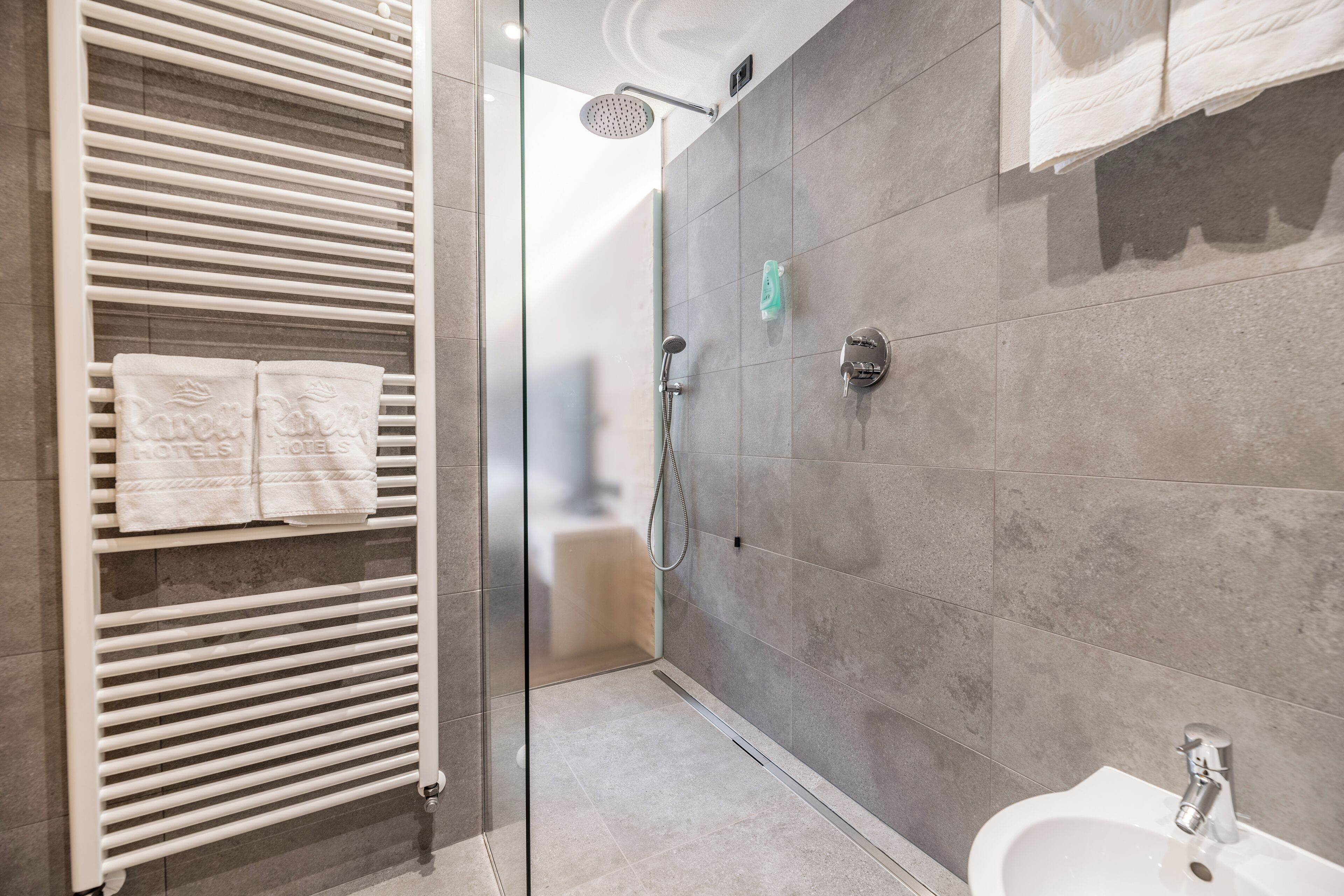 Un baño moderno con cabina de ducha de vidrio, un lavabo blanco y un perchero con toallas.