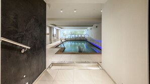 Ein moderner, überdachter Schwimmbereich mit klarem Wasser, einer dunklen Marmorwand an einer Seite und einem gefliesten Boden, der zum Pool führt.