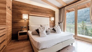 Ein Schlafzimmer mit Holzwand, einem großen Bett mit weißer Bettwäsche, zwei Nachttischlampen und Blick auf eine Berglandschaft durch eine Glastür.