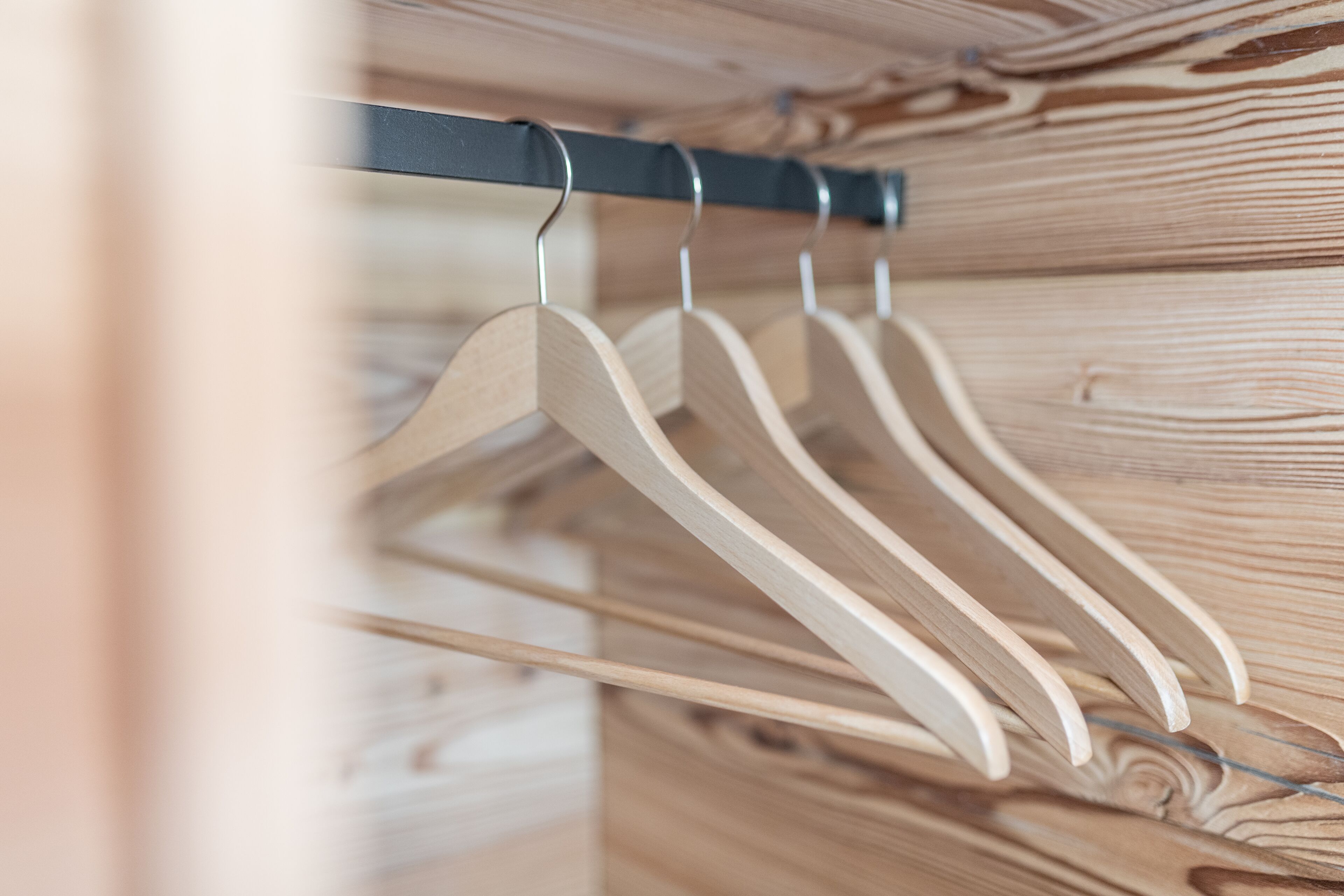 A wooden closet with a metal rod holding wooden hangers.