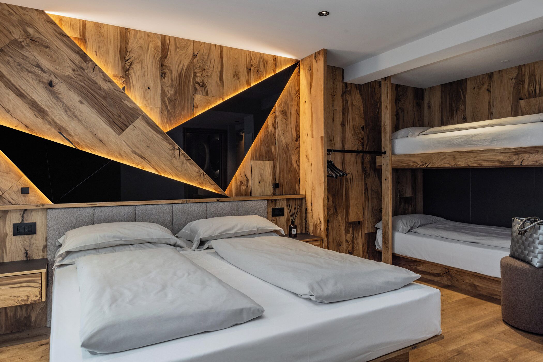 A modern bedroom with a central bed flanked by two bunk beds, wooden wall panels, and a geometric light fixture.